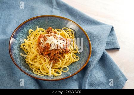 Spaghetti Bolognese, Pasta mit Sauce aus Hackfleisch und Tomaten, garniert mit Parmesan auf blauem Teller und Serviette, italienisches Gericht, Kopie Stockfoto