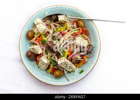 Griechischer Salat mit Zwiebeln, Paprika, Oliven, Feta und Kräutern in einer Schüssel, mediterranes vegetarisches Gericht auf einem weißen Tisch, Kopierraum, Blick aus einem hohen Winkel Stockfoto