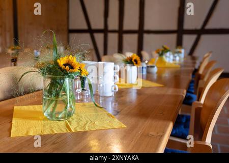 Lange Holztische, dekoriert mit Blumensträußen und Kaffeetassen für Treffen oder informelle Treffen eines Vereins in einem Fachwerkraum Stockfoto