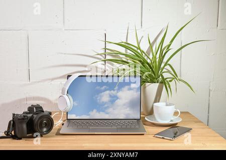 Laptop, Kamera, Kopfhörer und Smartphone auf einem hölzernen Schreibtisch, Büroarbeitsplatz eines Journalisten oder Fotografen vor einer weiß lackierten Wand, Kopie Stockfoto