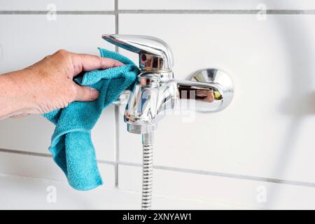 Reinigen eines Wannenarmators mit einem blauen Mikrofasertuch, um Kalkflecken aus hartem Kalziumwasser, Kopierraum, ausgewähltem Fokus und geringer Tiefe zu entfernen Stockfoto