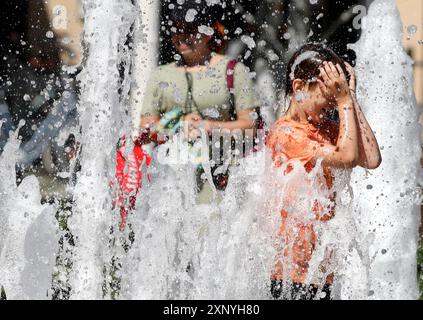 Ein Junge kühlt sich an einem Brunnen ab, Berlin, 30.07.2024. Deutschland Stockfoto