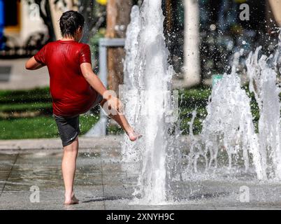 Ein Junge kühlt sich an einem Brunnen ab, Berlin, 30.07.2024. Deutschland Stockfoto