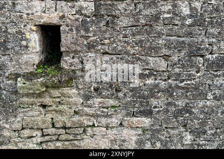 Stillleben zeigt eine alte, mittelalterliche Steinmauer mit einer kleinen, fensterartigen Öffnung in Frankreich. Stockfoto