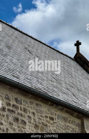 Das vertikale Stillleben zeigt eine antike, nicht identifizierbare mittelalterliche Steinkirche mit einem kleinen Kreuz auf dem Dach in Frankreich, die vor einem blauen Himmel steht. Stockfoto