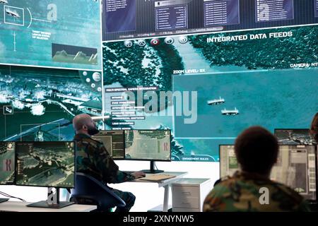 Militärangehörige überwachen Überwachungsbilder von Satellitensystemen auf Großbildschirmen im Kontrollraum und sammeln Informationen für eine neue Verteidigungsoperation. Soldaten arbeiten an der Aufklärung. Stockfoto