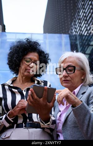 Niedriger Winkel. Verschiedene Geschäftsfrauen versammelten sich mit einem Tablet-pc im Freien. Stockfoto