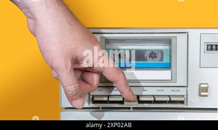 Vorderansicht der Hand eines Mannes, der den Schlüssel eines alten Aluminiumrekorders mit Musikkassette auf gelbem Hintergrund zerquetscht Stockfoto