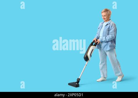 Reife Frau mit Staubsauger auf blauem Hintergrund Stockfoto