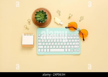 Moderne Computertastatur mit Zimmerpflanze, Sonnenbrille, Notebook und Flash-Laufwerk auf gelbem Hintergrund Stockfoto