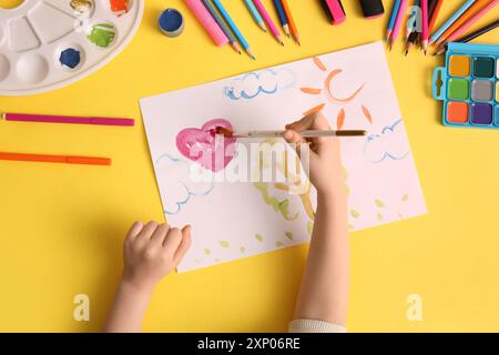 Kinderhandzeichnung Herz mit Pinsel, Farben und Bleistiften auf gelbem Hintergrund Stockfoto