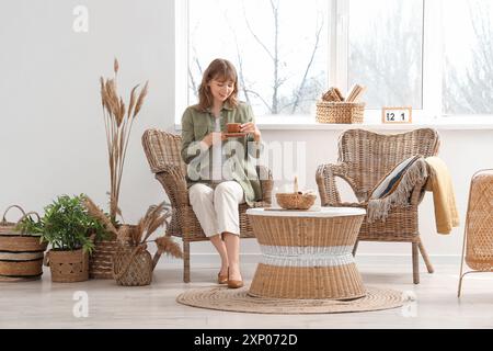 Junge hübsche Frau, die auf Sessel mit einer Tasse Kaffee im weißen Wohnzimmer sitzt Stockfoto