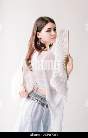 Die junge Frau strahlt Eleganz und Anmut in traditioneller asiatischer Kleidung aus und posiert mit weißen Fans in einem lebendigen Studio-Porträt. Ihre Schönheit und Ihr Selbstvertrauen Stockfoto