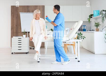 Männlicher Endokrinologe zeigt Schilddrüsenmodell bei weiblicher Patientin in der Klinik Stockfoto