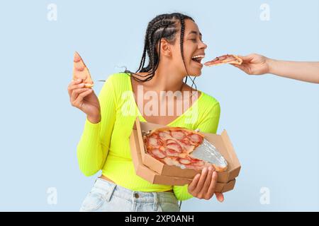 Junge afroamerikanische Frau, die leckere Peperoni-Pizza auf blauem Hintergrund isst Stockfoto