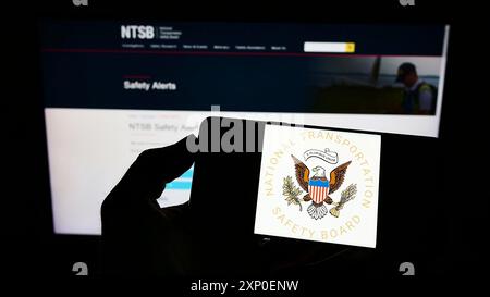 Stuttgart, Deutschland, 29.03.2022: Person, die ein Mobiltelefon mit dem Siegel des US National Transportation Safety Board (NTSB) auf dem Bildschirm vor der Webseite hält. Stockfoto