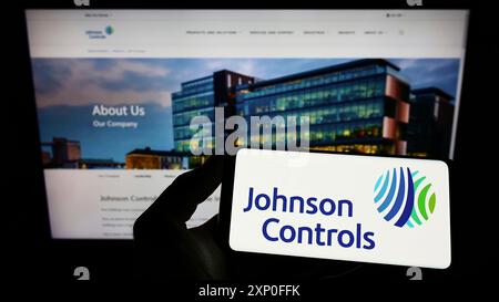 Stuttgart, Deutschland, 03.12.2022: Person, die ein Mobiltelefon mit dem Logo der Firma Johnson Controls International plc (JCI) auf dem Bildschirm vor der Webseite hält. Stockfoto