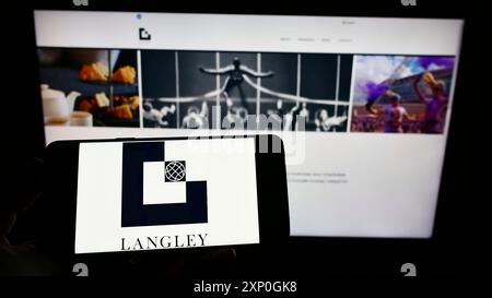 Stuttgart, 26.02.2022: Person, die ein Mobiltelefon mit dem Logo des britischen Ingenieurunternehmens Langley Holdings plc auf dem Bildschirm vor der Webseite hält. Stockfoto