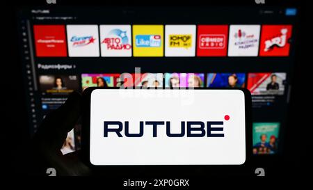 Person, die ein Smartphone mit dem Logo der russischen Videoplattform Rutube auf dem Bildschirm vor der Website hält. Schwerpunkt auf dem Display des Telefons Stockfoto