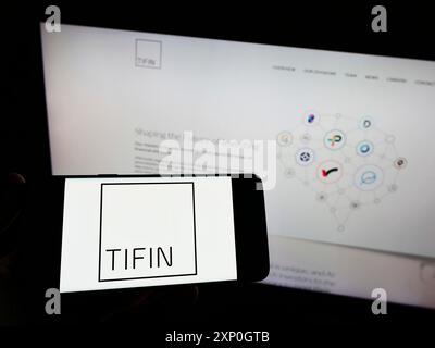 Person mit Smartphone und Logo der US-Investmentberatungsgesellschaft Tifin LLC auf dem Bildschirm vor der Website. Schwerpunkt auf dem Display des Telefons Stockfoto