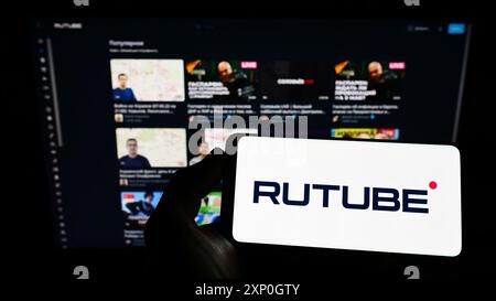 Person, die ein Mobiltelefon mit dem Logo der russischen Video-Streaming-Plattform Rutube auf dem Bildschirm vor der Webseite hält. Schwerpunkt auf dem Display des Telefons Stockfoto