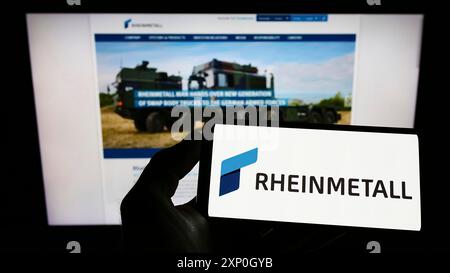 Person mit Smartphone und Logo der deutschen Verteidigungsfirma Rheinmetall AG auf dem Bildschirm vor der Website. Schwerpunkt auf dem Display des Telefons Stockfoto