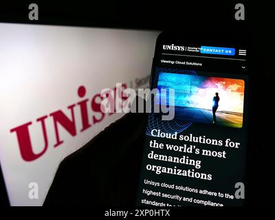 Stuttgart, Deutschland, 02.06.2022: Person, die ein Mobiltelefon hält, mit Webseite des US-amerikanischen IT-Unternehmens Unisys Corporation vor dem Firmenlogo. Fokus Stockfoto