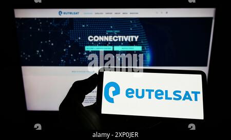 Stuttgart, Deutschland, 01-30-2022: Person, die ein Mobiltelefon mit dem Logo des französischen Satellitenunternehmens Eutelsat S.A. auf dem Bildschirm vor der Webseite der Firma hält. Stockfoto