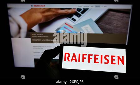 Stuttgart, Deutschland, 29.01.2022: Person mit Handy mit Logo der Schweizer Bank Raiffeisen Schweiz Genossenschaft auf dem Bildschirm vor dem Geschäft Stockfoto