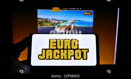 Stuttgart, Deutschland, 01-08-2022: Person, die ein Mobiltelefon mit dem Logo der transnationalen europäischen Lotterie Eurojackpot auf dem Bildschirm vor dem Geschäft hält Stockfoto