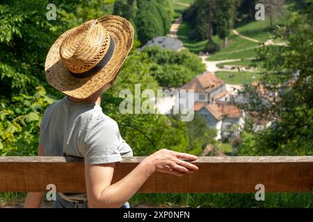 Frau mit braunen Haaren, grauem T-Shirt, Jeans und Strohhut, die auf einer Parkbank in der Sonne sitzt und auf den Staatspark Fürstenlager, Auerbach, Bensheim blickt Stockfoto