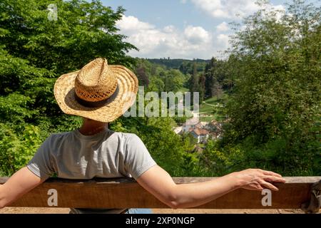Frau mit Strohhut, grauem T-Shirt und Jeans sitzt auf einer Parkbank in der Sonne und blickt auf den Staatspark Fürstenlager, Auerbach, Bensheim Stockfoto