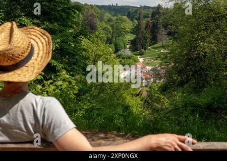 Frau mit Strohhut, grauem T-Shirt und Jeans sitzt auf einer Parkbank in der Sonne und blickt auf den Staatspark Fürstenlager, Auerbach, Bensheim Stockfoto