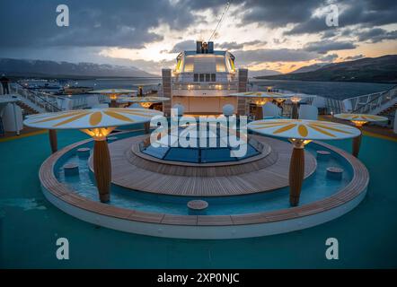 Beleuchtetes Bootsdeck des AIDA Bella Kreuzfahrtschiffs am Abend, Fjord mit Gebirgszügen Islands im Hintergrund, Weitwinkelaufnahme Stockfoto