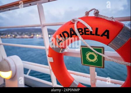 Nahaufnahme orangefarbener Rettungsschirm des Kreuzfahrtschiffs AIDA Bella, das am Abend am Schiffs-Geländer befestigt ist, mit der Stadt Island im Hintergrund Stockfoto