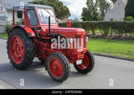 Roter Vintage-Traktor, sorgfältig restaurierter Oldtimer, Fahrt auf der Straße durch das Dorf, Bewegung bluer, ausgewählter Fokus Stockfoto