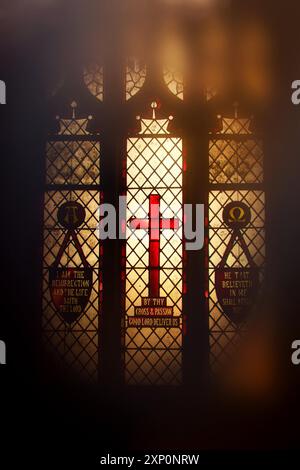 Kirchenfenster aus Buntglas mit einem markanten roten Kreuz, beleuchtet von hinten Stockfoto