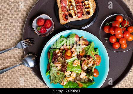 Ein lebhaftes, verführerisches Frühstück mit bunten Salaten, Garnelen, Reifen Tomaten, Sandwiches, Bananen, frische Erdbeeren. Gesunde Mahlzeit bietet ein köstliches Nutri Stockfoto