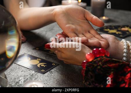 Wahrsagerin liest Zeilen auf Frauenpalme am schwarzen Tisch, Nahaufnahme. Chiromantie Stockfoto