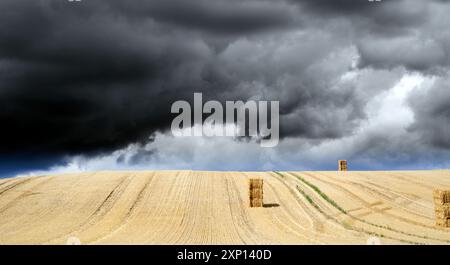 Schwere, dunkle Gewitterwolken über einem hellen Stoppelfeld mit Strohballen Stockfoto