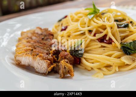 Thailändische Spaghetti mit getrockneter Chilisauce und heißen, zarten und köstlichen Schweinekoteletts werden auf einem weißen Teller auf einem Holztisch, resu, serviert Stockfoto