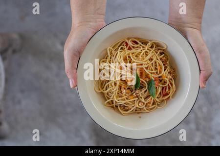 Gebratene Spaghetti mit Tomatensauce und Hähnchenfleisch in heißem Thai-Stil. Zart und köstlich serviert auf einem weißen Teller auf einem Holztisch, Re Stockfoto