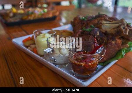 Deutsche Schweinshaxe wird mit gebackenen Kartoffeln und Sauce auf einer weißen Keramikplatte serviert, die auf dem Esstisch platziert wird, damit die Schweinshaxe gelesen wird Stockfoto