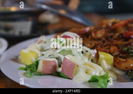 Fruchtsalat ist ein Dessert aus verschiedenen Obstscheiben, garniert mit einem Dressing und serviert auf einem großen Steakteller für Gäste Stockfoto