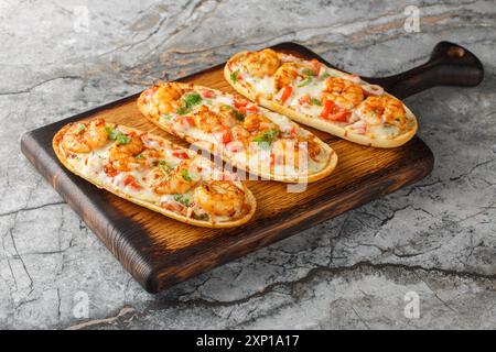 Köstliche heiße offene Sandwiches mit Garnelen, Käse, Knoblauch und Tomaten aus nächster Nähe auf einem Holzbrett auf dem Tisch. Horizontal Stockfoto