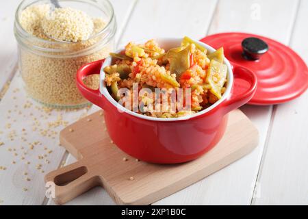 Hirsebrei mit grünen Bohnen und Tomaten in rotem Topf auf einem rustikalen Tisch Stockfoto