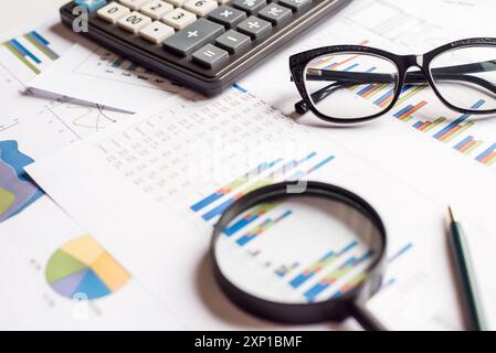 Große Sicht auf das Vergrößerungsglas mit Geschäftstabelle, Rechner, Brille und Stift Stockfoto