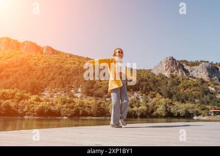 Frau, Fluss, Berg - Frau in gelber Jacke, die am Fluss mit Bergen im Hintergrund läuft Stockfoto