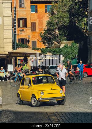 Ein gelbes Auto parkt auf einer Kopfsteinpflasterstraße vor einem Gebäude. Die Straße ist voll mit Leuten, die herumlaufen und Autos parken. Die Szene hat einen Stockfoto