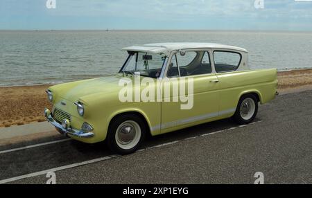 Klassischer gelber Ford Anglia-Motor an der Strandpromenade Strand und Meer im Hintergrund. Stockfoto